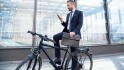 Mann mit dem Fahrrad auf dem Weg zur Arbeit schaut auf sein Smartphone.